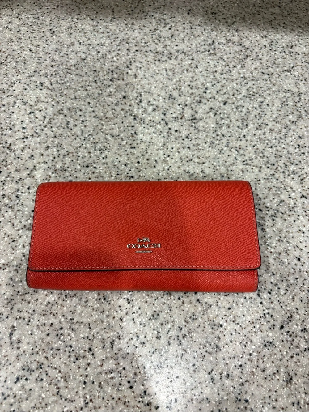 Coach Slim Trifold Wallet in a vibrant coral or orange color